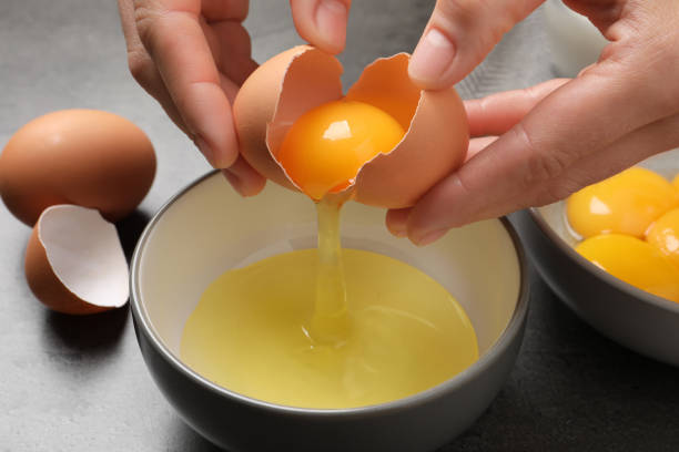 istock Woman separating egg yolk from white over bowl at grey table, closeup 1405646750