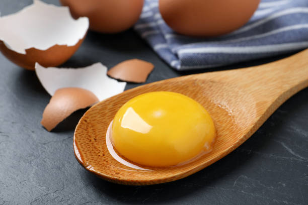 istock Wooden spoon with raw egg yolk on black table, closeup 1405646766