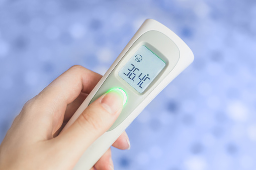 Female hand holding a modern infrared thermometer isolated over blue textile background. Distant measurement of body temperature. Control of infectious diseases. Health care during seasonal illnesses