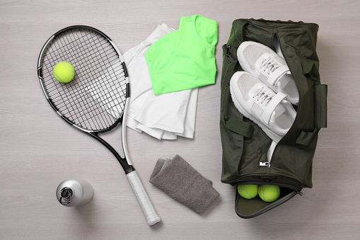 Sports bag and tennis equipment on wooden background, flat lay