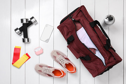 Gym bag and sports equipment on white wooden background, flat lay