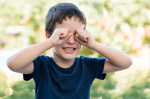 Child suffering itching scratching eyes outdoors in a park