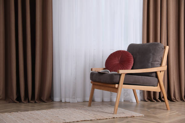 istock Comfortable armchair with cushion near window indoors, space for text. Interior design 1405648811