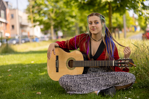 LGBTQ+ young woman playing guitar outdoors, with alternative hairstyle as self-expression giving confidence to be accepted