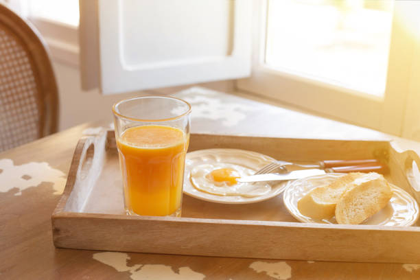 frühstücksthema. ein glas orangensaft und ein spiegelei mit toast stehen auf einem holztablett auf dem tisch in der nähe des von der sonne beleuchteten fensters. - frühstücksbereich stock-fotos und bilder