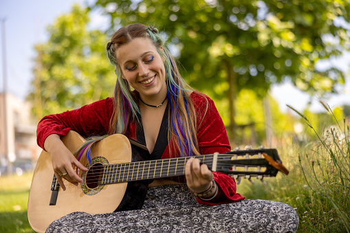 LGBTQ+ young woman playing guitar outdoors, with alternative hairstyle as self-expression giving confidence to be accepted