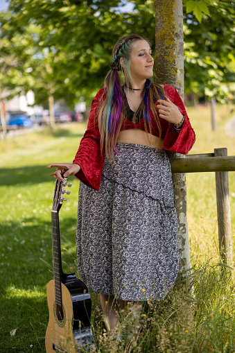 LGBTQ+ young woman playing guitar outdoors, with alternative hairstyle as self-expression giving confidence to be accepted