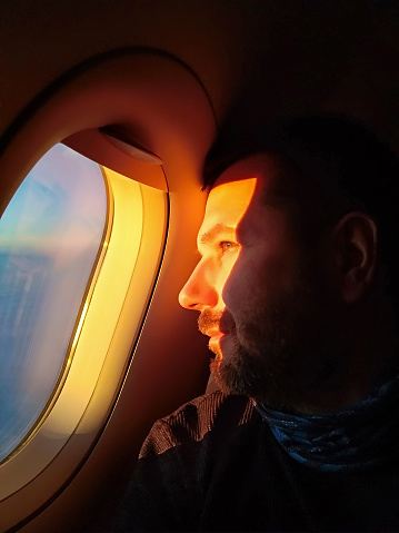 man looks out the porthole of the plane