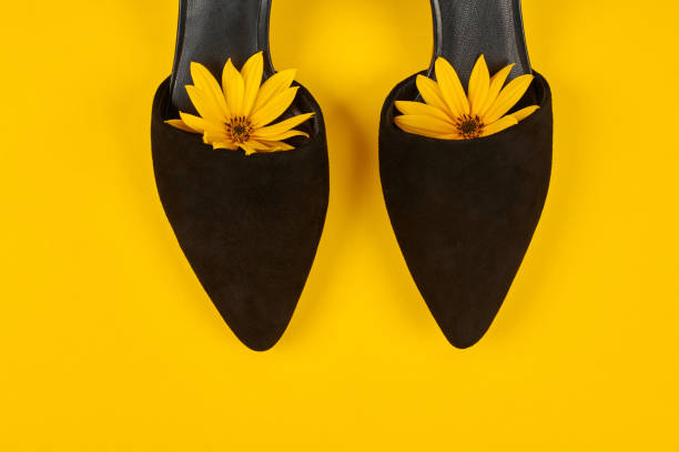 sapatos de corte pretos de camurça com broto de flor topinambura amarelo dentro do dedo do pé, fundo amarelo, feminilidade - womanhood - fotografias e filmes do acervo