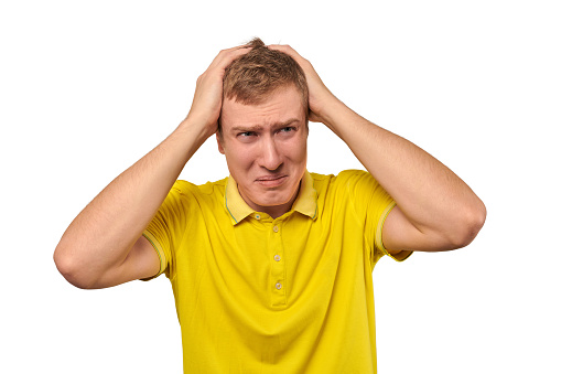 Upset man in yellow T-shirt clutched at his head, forgetful man with headache isolated on white background. Young guy worried and frustrated, grabbed his head, sharp severe headache