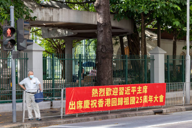 The 25th anniversary of the handover of Hong Kong from Britain to China Hong Kong - June 28, 2022 : A man stands next to a banner with a message to welcome Chinese President Xi Jinping in Happy Valley, Hong Kong. xi jinping stock pictures, royalty-free photos & images