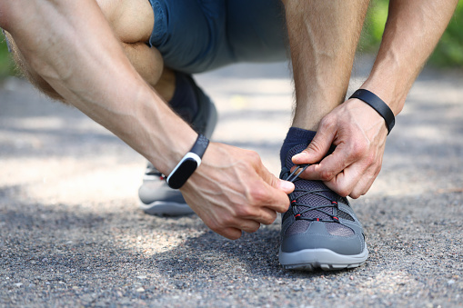 Close-up of sporty male person hands tying up shoelace. Stylish grey sneakers for running. Man ready for morning run. City street. Workout and training for strong body concept