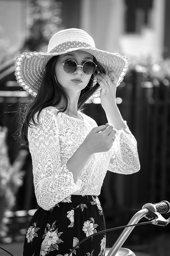 serious beautiful girl in sunhat and sunglasses and bike looking at camera in sun rays, monochrome