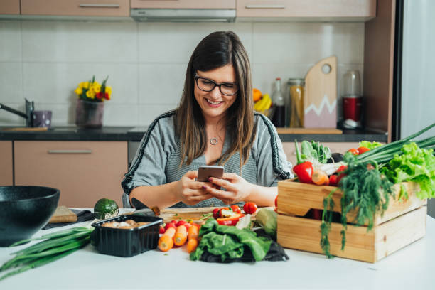 istock Happy Woman Using Mobile Phone while Making Healthy Lunch in the Kitchen 1405666362