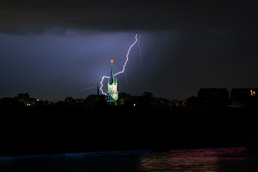 Dramatic scene where lightning strikes down just behind a church at night. Location is near the town of Druten at the river Waal in The Netherlands.