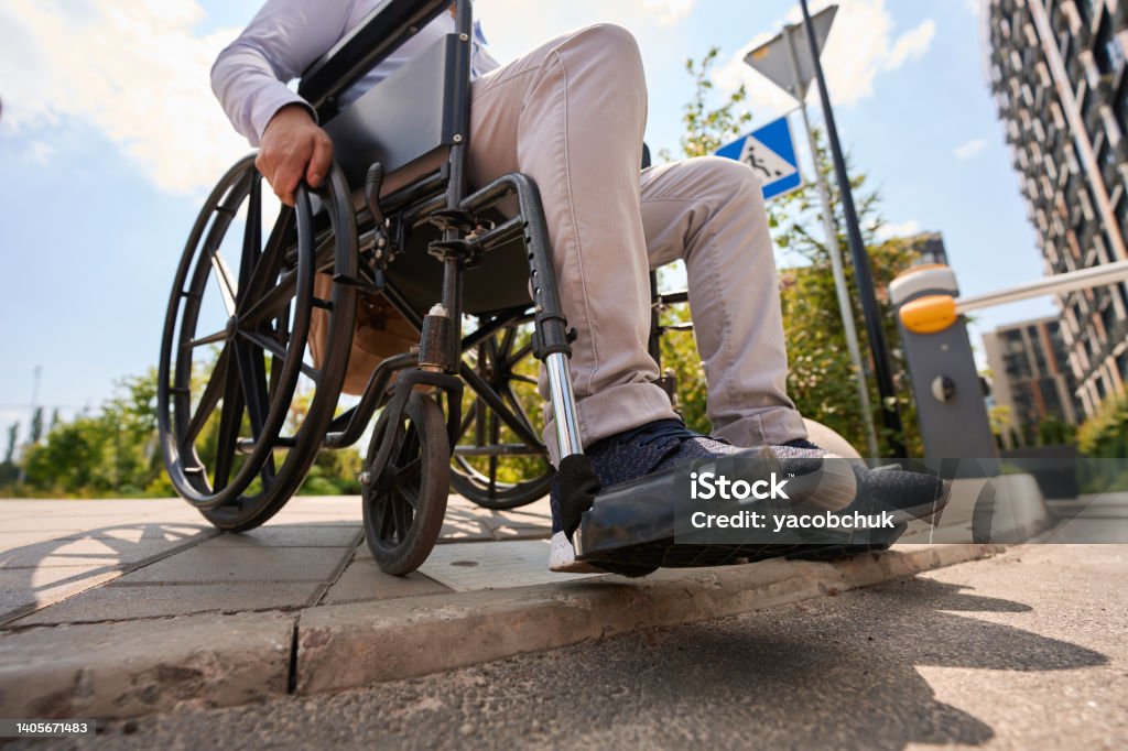 Disabled man going down curb in manual wheelchair Cropped photo of male sitting in wheel chair on edge of pavement Wheelchair Stock Photo