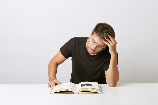 Young student reading and studying for an exam, reoisado su
head on hand, on white background and white table.