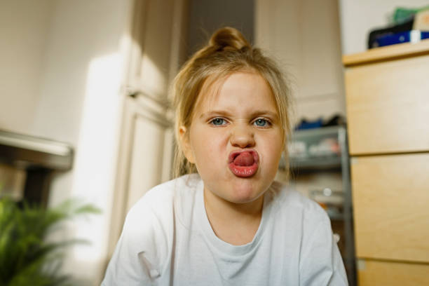 istock Girl 3-year-old at home on floor grimaces, makes faces at camera 1405674592