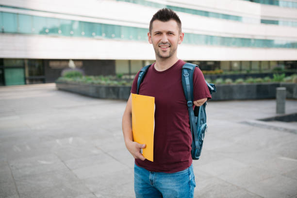 Happy male adult student standing in front of the university stock photo