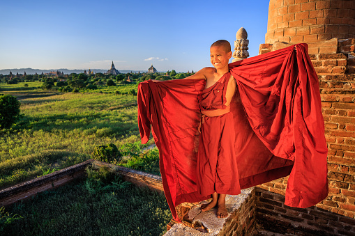Young Buddhist monk putting on robe on one of ancient temples in Bagan, Myanmar