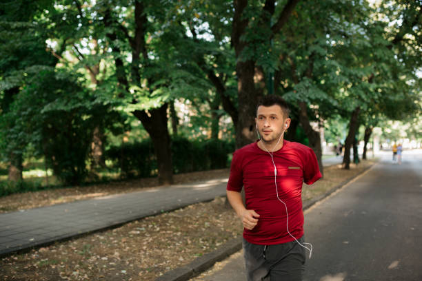 Young man with an amputated arm staying in shape by jogging in the city and listening to music while having his earphones on