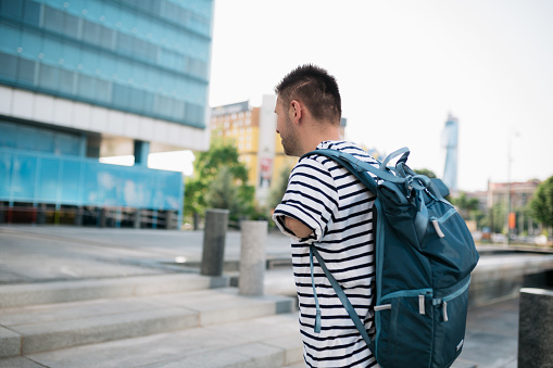 Behind view of an adult university student with physical disability, an amputated arm, walking to the educational building while carrying the backpack