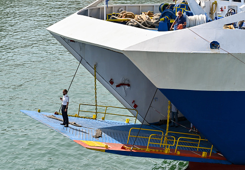 Piraeus, Athens, Greece - June 2022: Ship's officer standing on the vehicle ramp of a car ferry guiding the ship into dock.