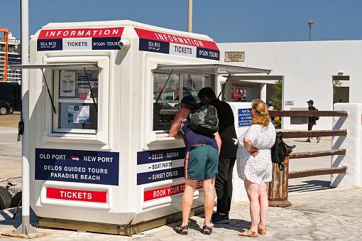 Mykonos, Greece - June 2022: People queuing to buy ferry tickets from a kiosk on the harbour of the Greek Island of Mykonos.