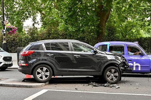 London, England - June 2022: Car with extensive damage to its front after colliding wityh a traffic light. The traffic light is wedged under the vehicle.