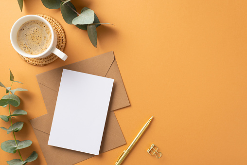 Business concept. Top view photo of workspace paper sheet over craft paper envelopes gold pen cup of coffee on rattan serving mat and eucalyptus on isolated orange background with blank space