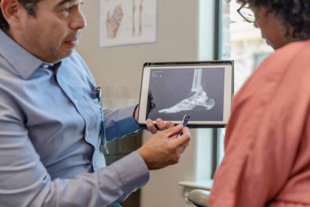 doctor, holding tablet displaying foot x-ray, listens to woman - podiatrist podiatry orthopedic surgeon human foot imagens e fotografias de stock