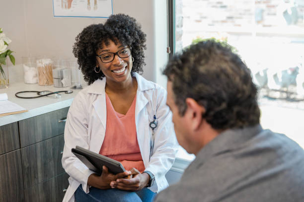 holding digital tablet, female doctor smiles encouragingly at male patient - male nurse black nurse doctor imagens e fotografias de stock