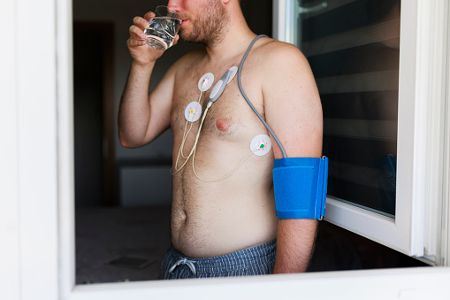 Man with cardio monitor drinking water, study of the work of the heart, cardiology. Holter monitor. Medical diagnostics. Health care, hospital. ECG sensors - electrocardiogram and blood pressure measurement.