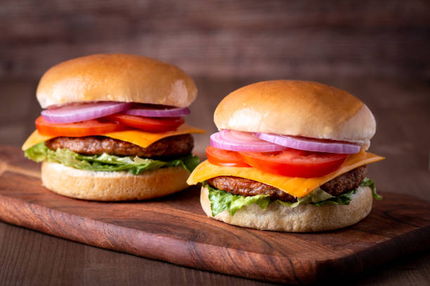 istock Two beef burgers with tomato and cheese on wooden board 1405684992