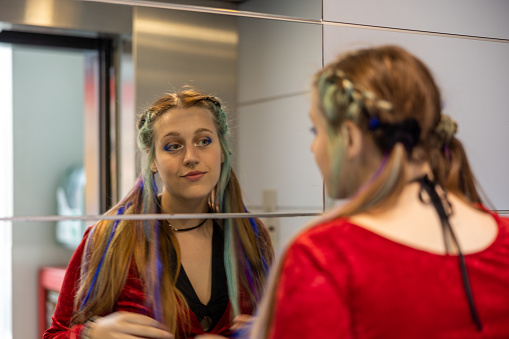 LGBTQ+ influencer girl checking herself in the mirror of an elevator, showing off her alternative hairstyle