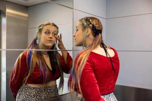 LGBTQ+ influencer girl checking herself in the mirror of an elevator, showing off her alternative hairstyle