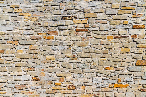 A fragment of a city wall of hewn stone on cement mortar. Stones of different sizes and colors, but in the same style.