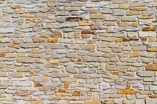 A fragment of a city wall of hewn stone on cement mortar. Stones of different sizes and colors. A fragment of a city wall of hewn stone on cement mortar. Stones of different sizes and colors, but in the same style. roughhewn stock pictures, royalty-free photos & images