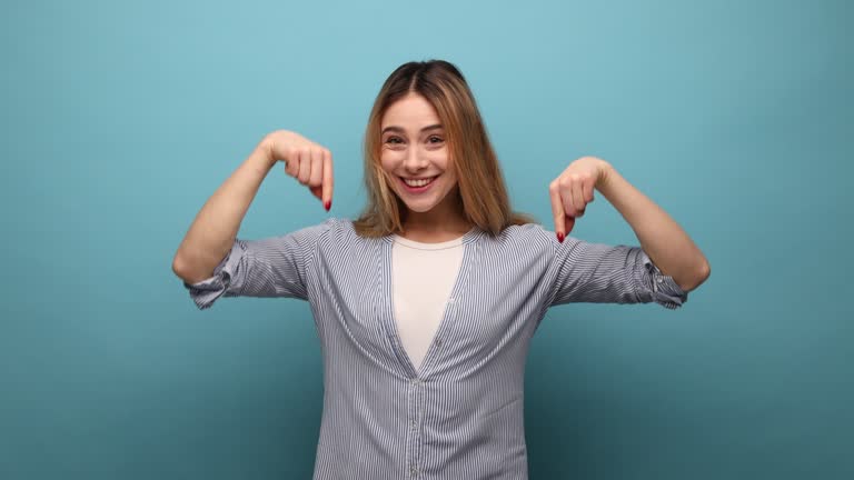 Positive woman pointing down place for commercial idea, looking at camera with toothy smile.