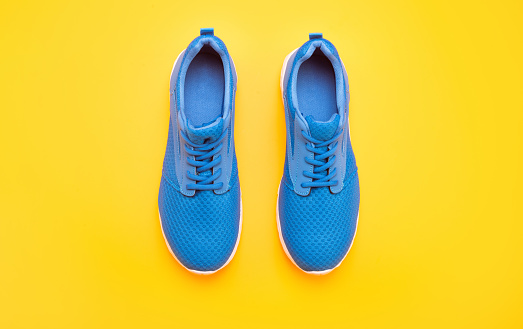 sporty blue sneakers pair on yellow background, footwear.