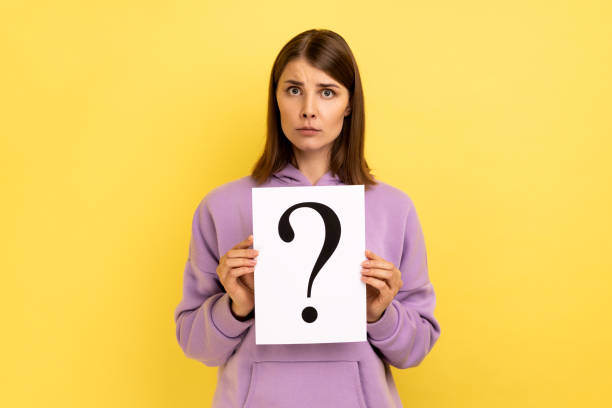 istock Woman looking at camera, holding paper with question mark, thinks about tasks. 1405696002