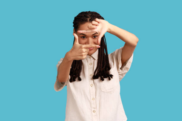 istock Woman makes hand frames, searches perfect angle, smiling, gazes at camera through hands. 1405696084
