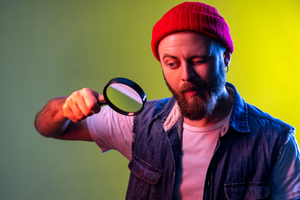 hipster man looking through magnifying glass, spying finding out something, exploring and inspecting - loupe quality control magnification glass imagens e fotografias de stock