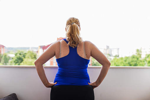 Woman in sports clothes standing on a balcony and doing exercises, close-up