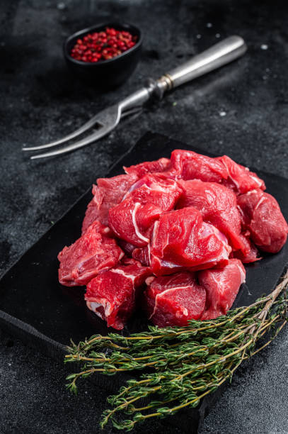 istock Raw diced red beef meat for Goulash on marble board. Black background. Top view 1405699000