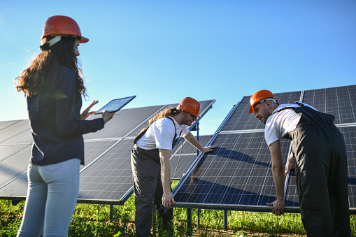 Rear View Of Female Engineer And Workers Manually Correcting Position Of Solar Panel
