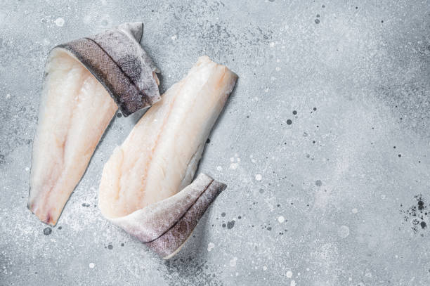 istock Two raw haddock fish fillets on kitchen table. Gray background. Top view. Copy space 1405699244