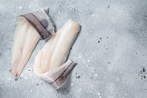 Two raw haddock fish fillets on kitchen table. Gray background. Top view. Copy space.