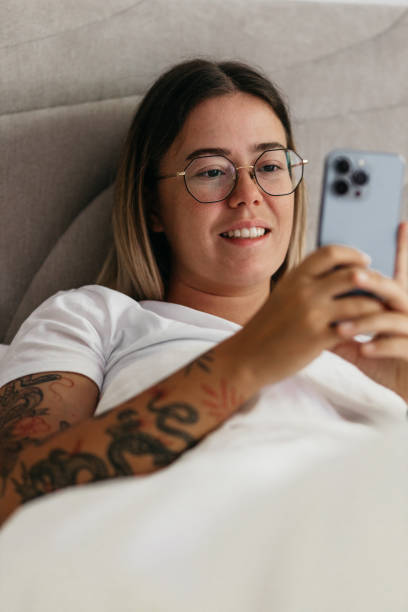 istock Attractive young woman with tattoos on her arm using her phone in bed 1405701233