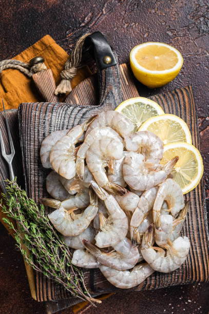 istock Raw tiger white shrimp prawn on board with herbs. Dark background. Top view 1405701241